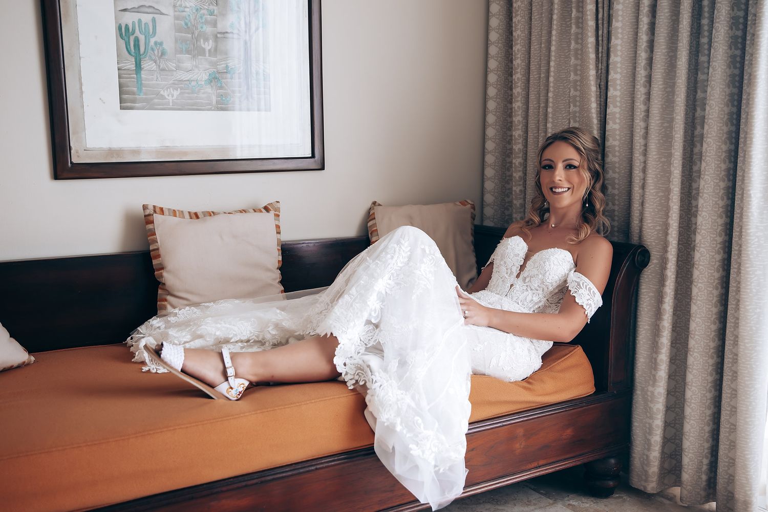 A bride in a white wedding dress reclines on a chaise lounge during preparation.