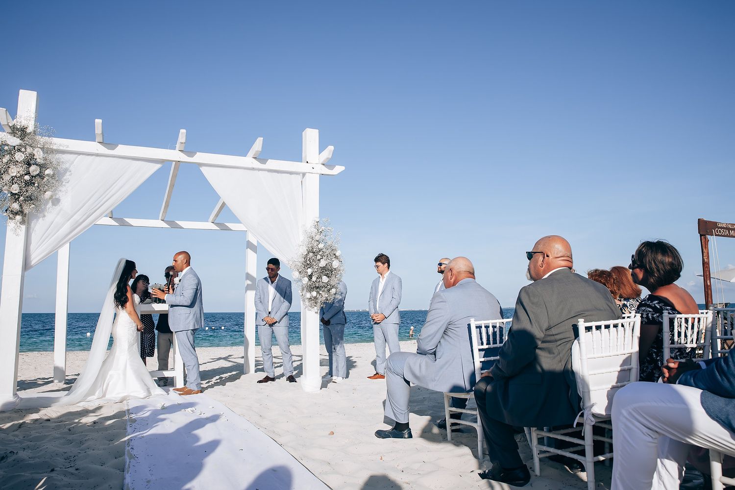 White wedding arch setup on beach with chairs and ocean view.