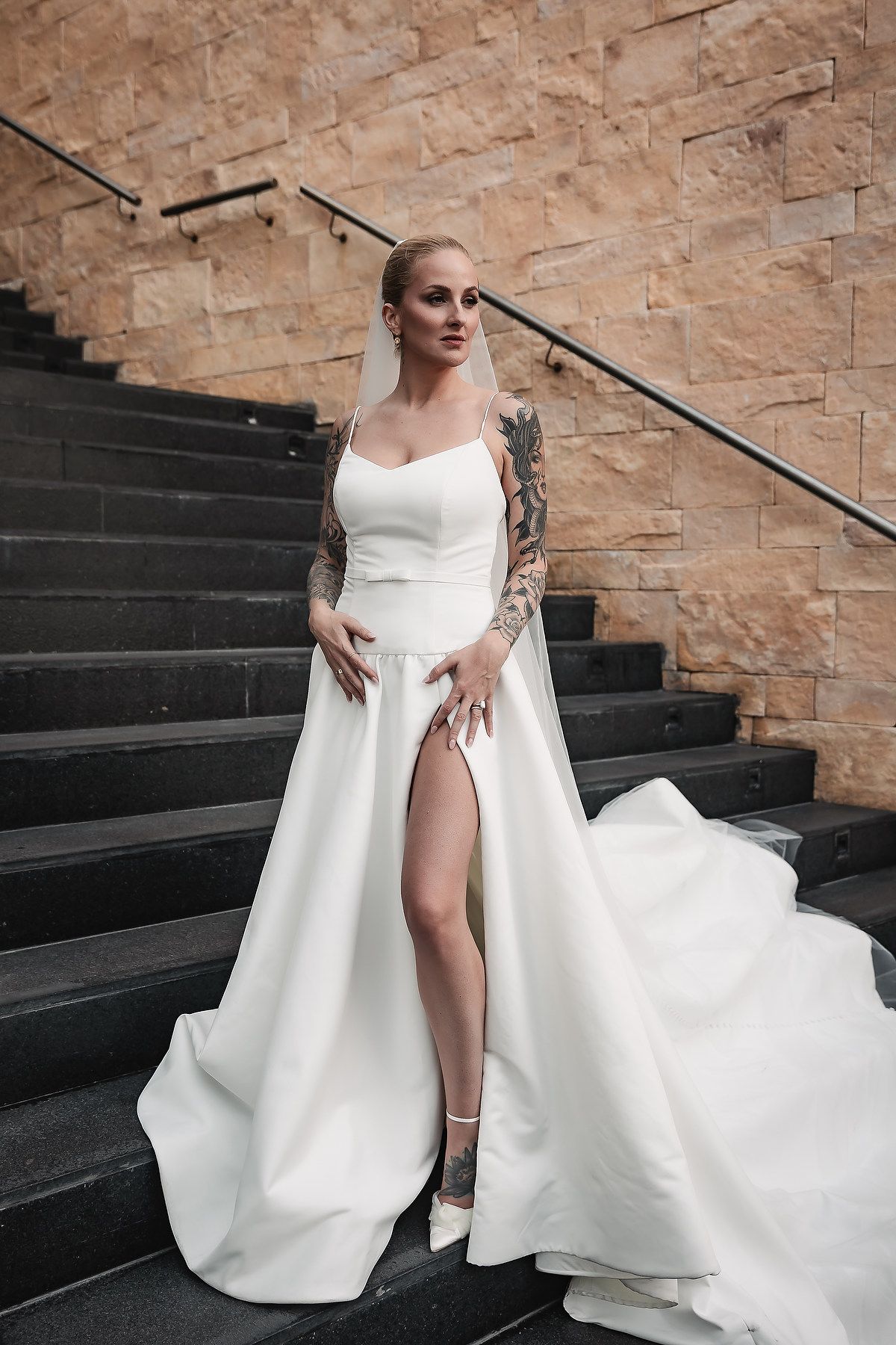Elegant white wedding gown with flowing train displayed on stone steps.
