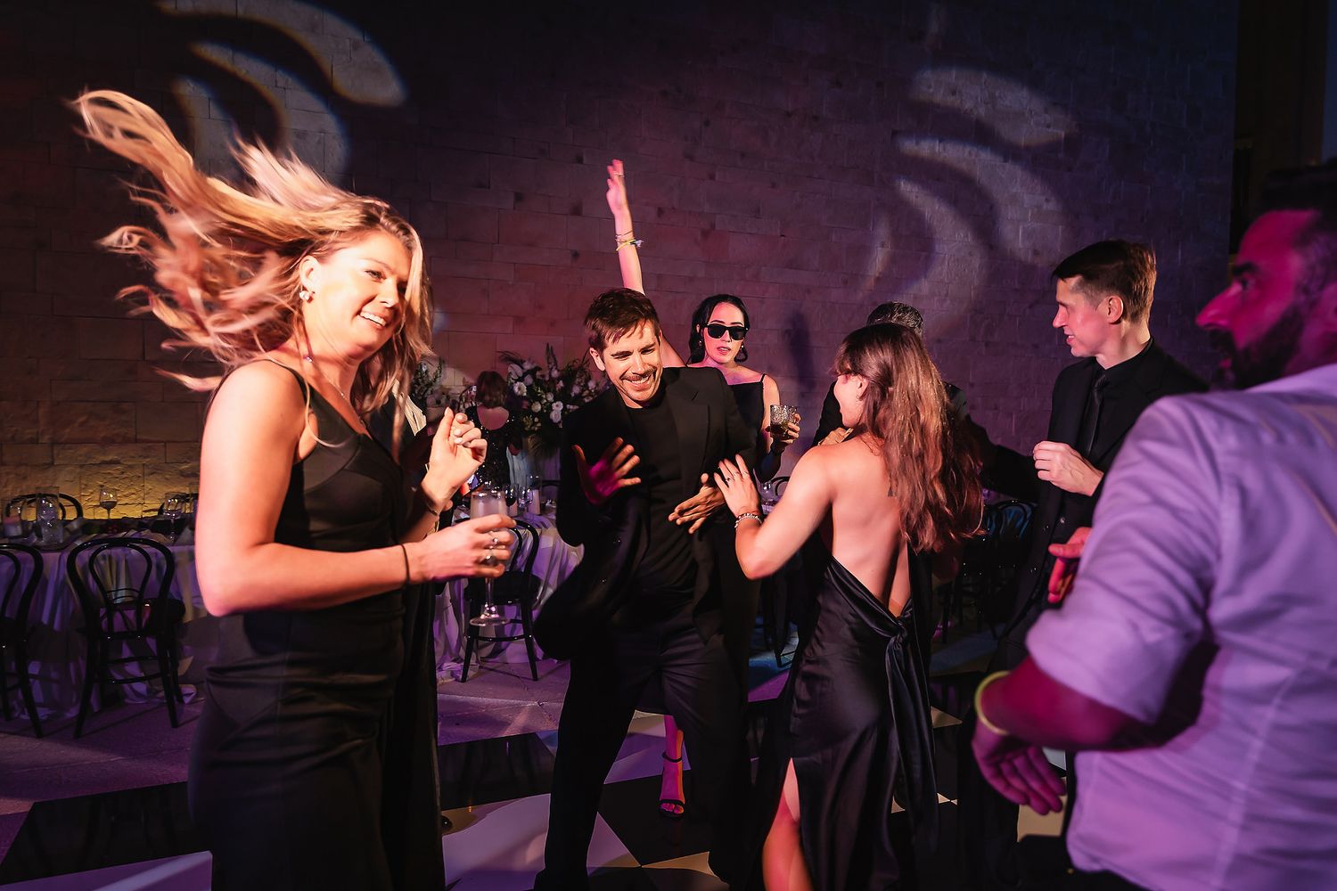 People dancing and socializing at a nightclub with purple lighting and dark ambiance.
