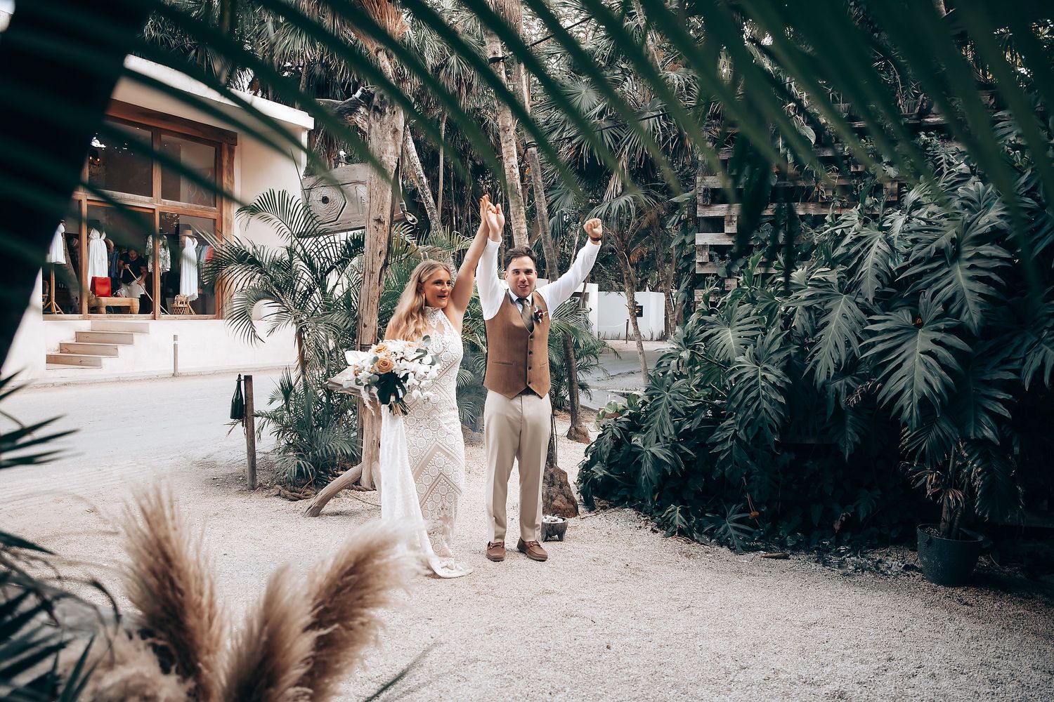 A couple walks through a lush tropical garden pathway during a wedding ceremony.