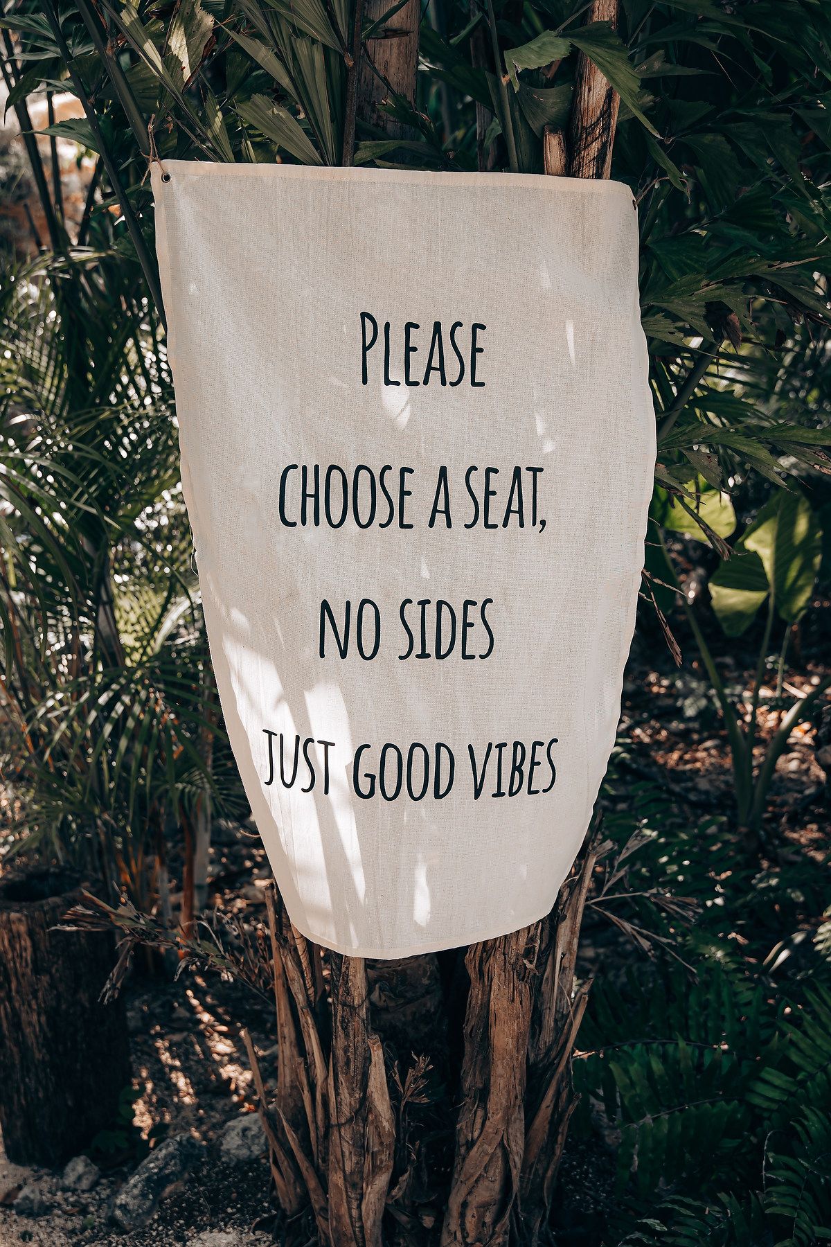 A series of white signs with handwritten messages including 'Please choose a seat' and 'Just good vibes' against dark foliage.