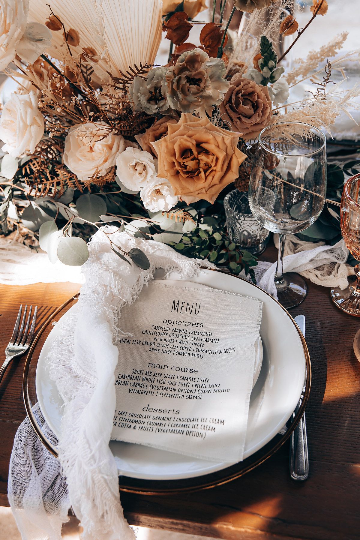 Wedding reception table details showing menu cards, place settings, and romantic dried floral decorations.