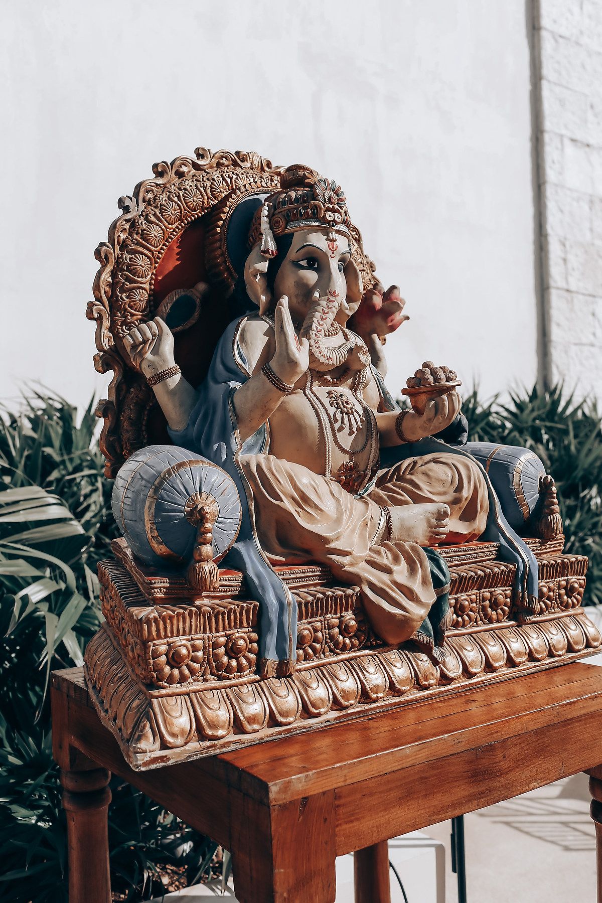 Ornate carved wooden bench with decorative details and cushions in an outdoor setting.