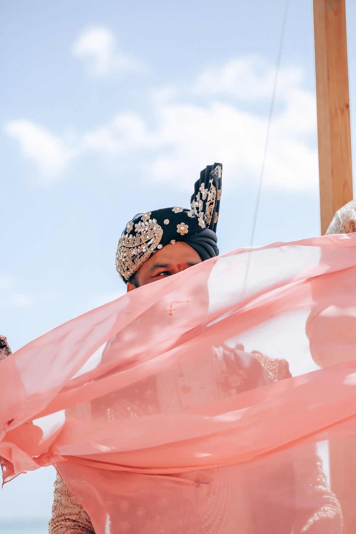Pink fabric billowing in the wind against a bright blue sky at an outdoor ceremony.