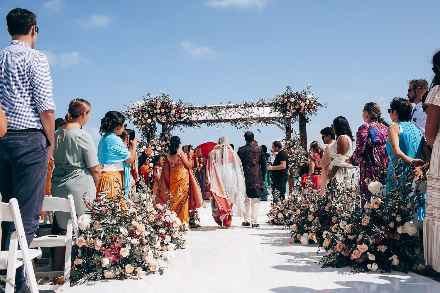 Wide angle view of a beach wedding ceremony with guests seated under a floral arch.