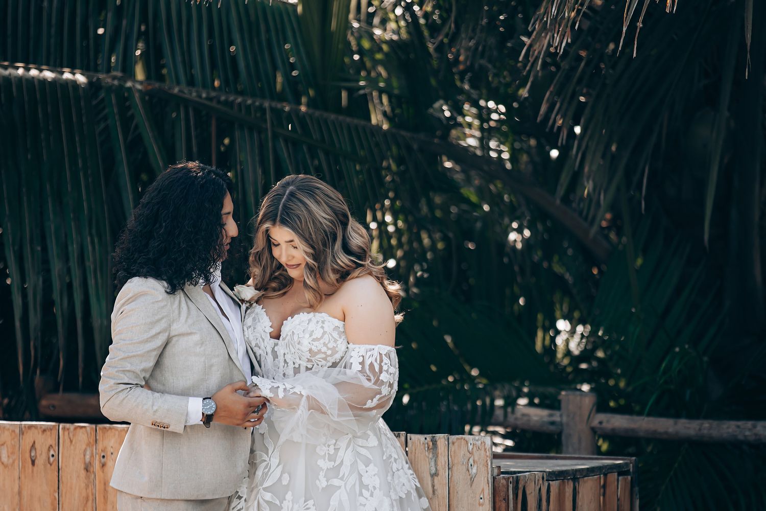 A romantic wedding moment captured on a rustic wooden deck surrounded by lush tropical foliage.