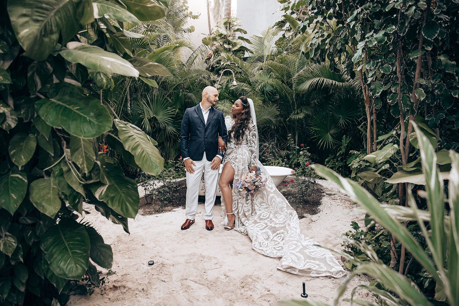 A romantic couple strolls along a garden path surrounded by lush tropical plants and greenery.