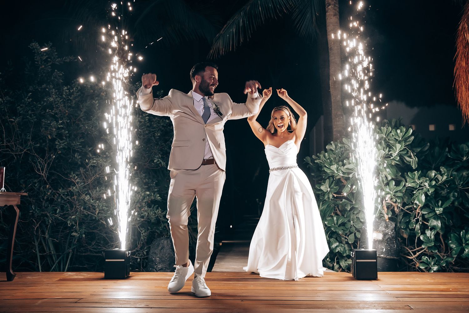 Wedding couple dances under sparkling fireworks at an outdoor nighttime reception celebration.
