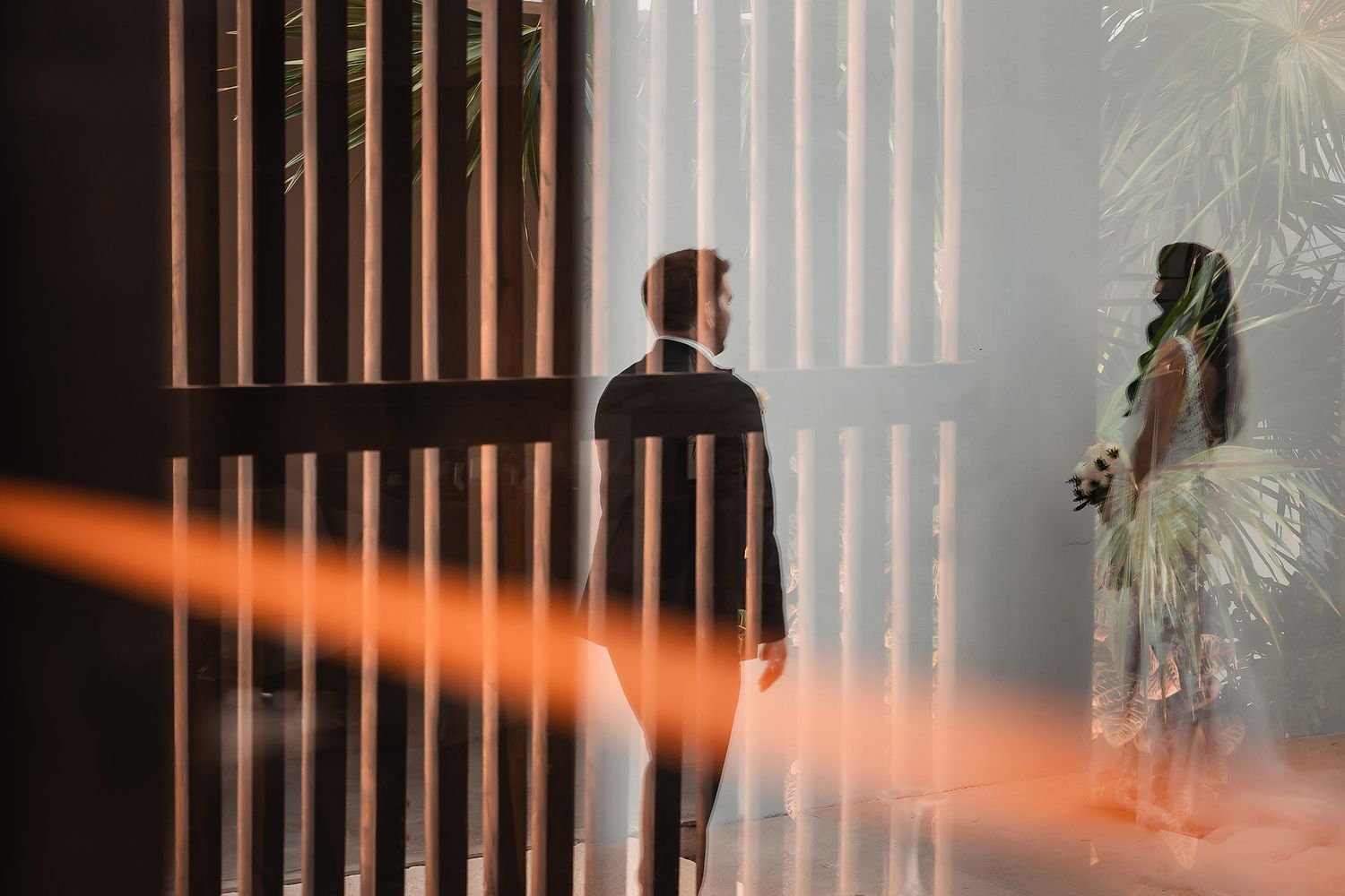 A couple shares an intimate moment in front of window blinds casting dramatic shadows.