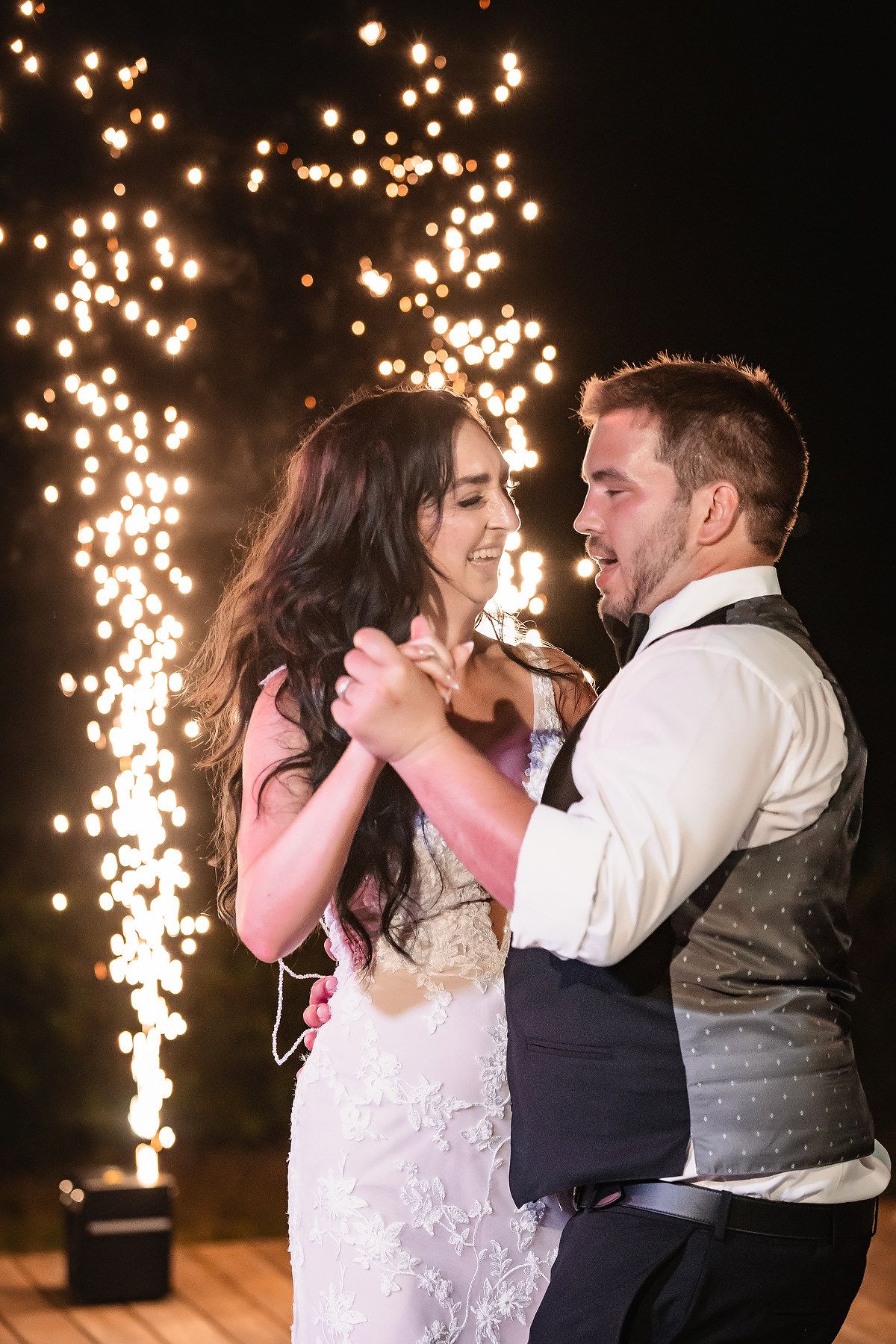 Couples dance joyfully under twinkling string lights at wedding reception.