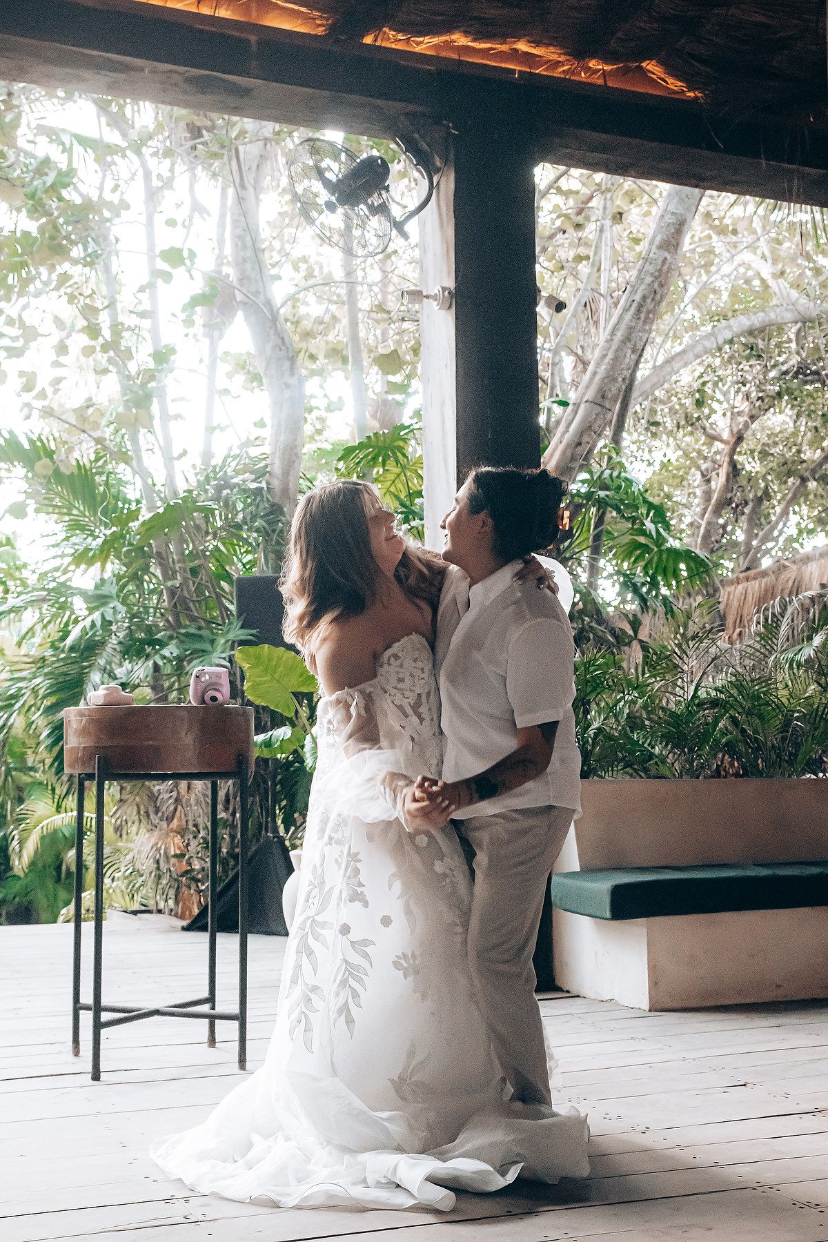 A romantic wedding couple sits together on a covered patio overlooking a tropical garden setting.