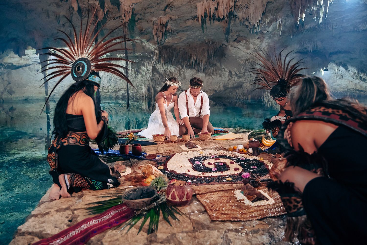 People relaxing on stone ledges inside a dimly lit cave with crystal clear turquoise waters below.