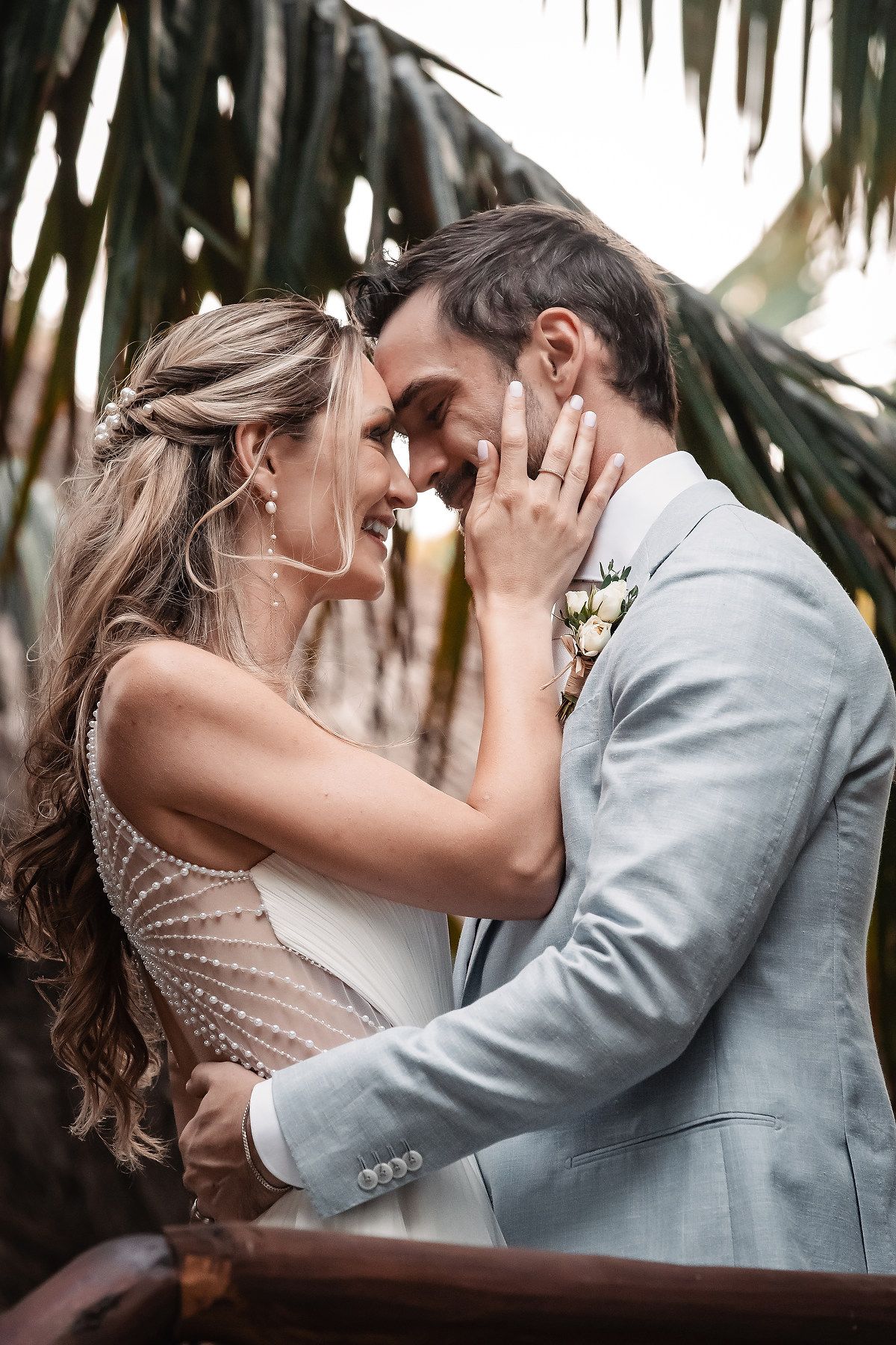 Romantic couple embraces beneath palm trees during a tropical beach photoshoot.