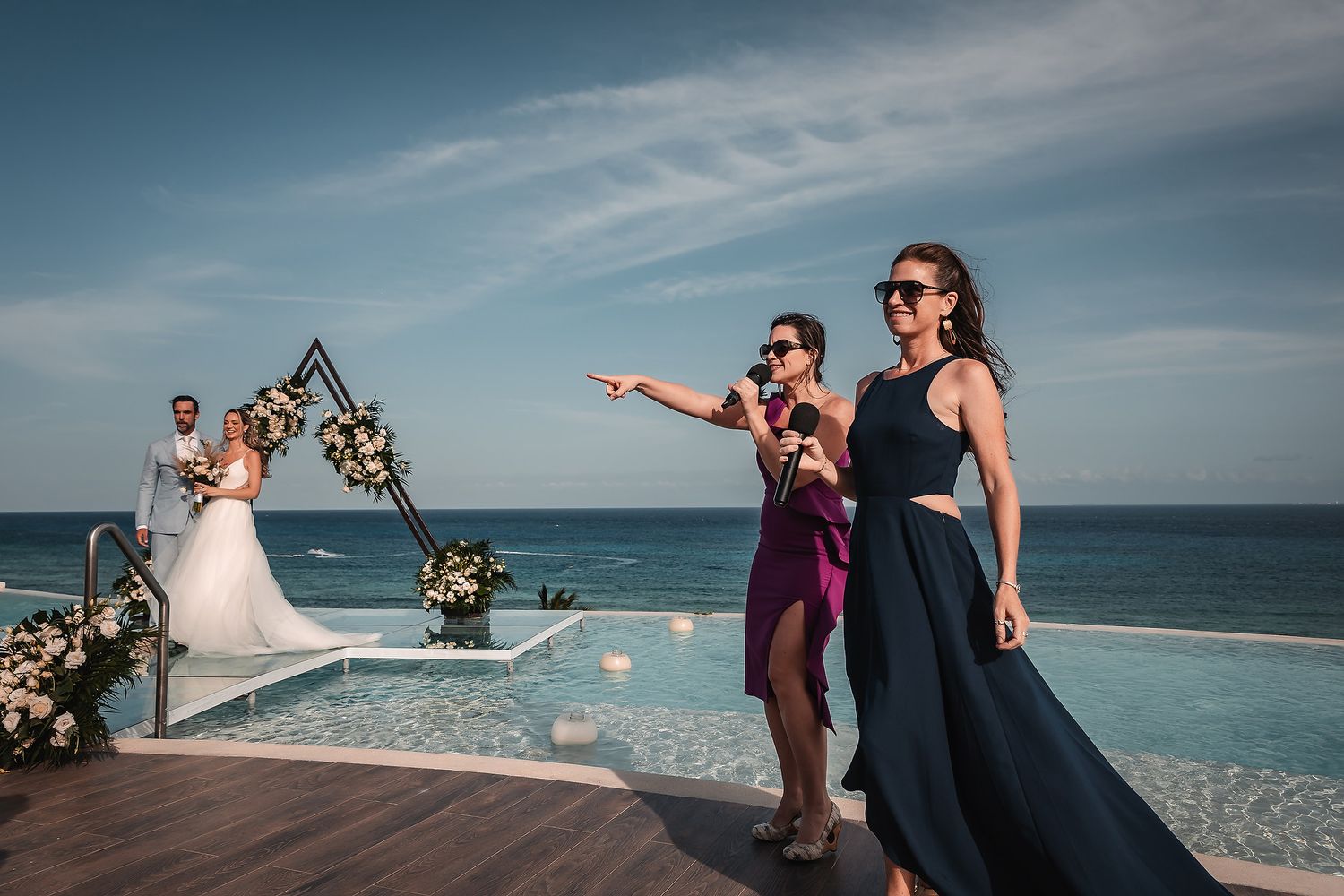 Wedding guests watching ceremony from deck with ocean view and floral triangle arch.