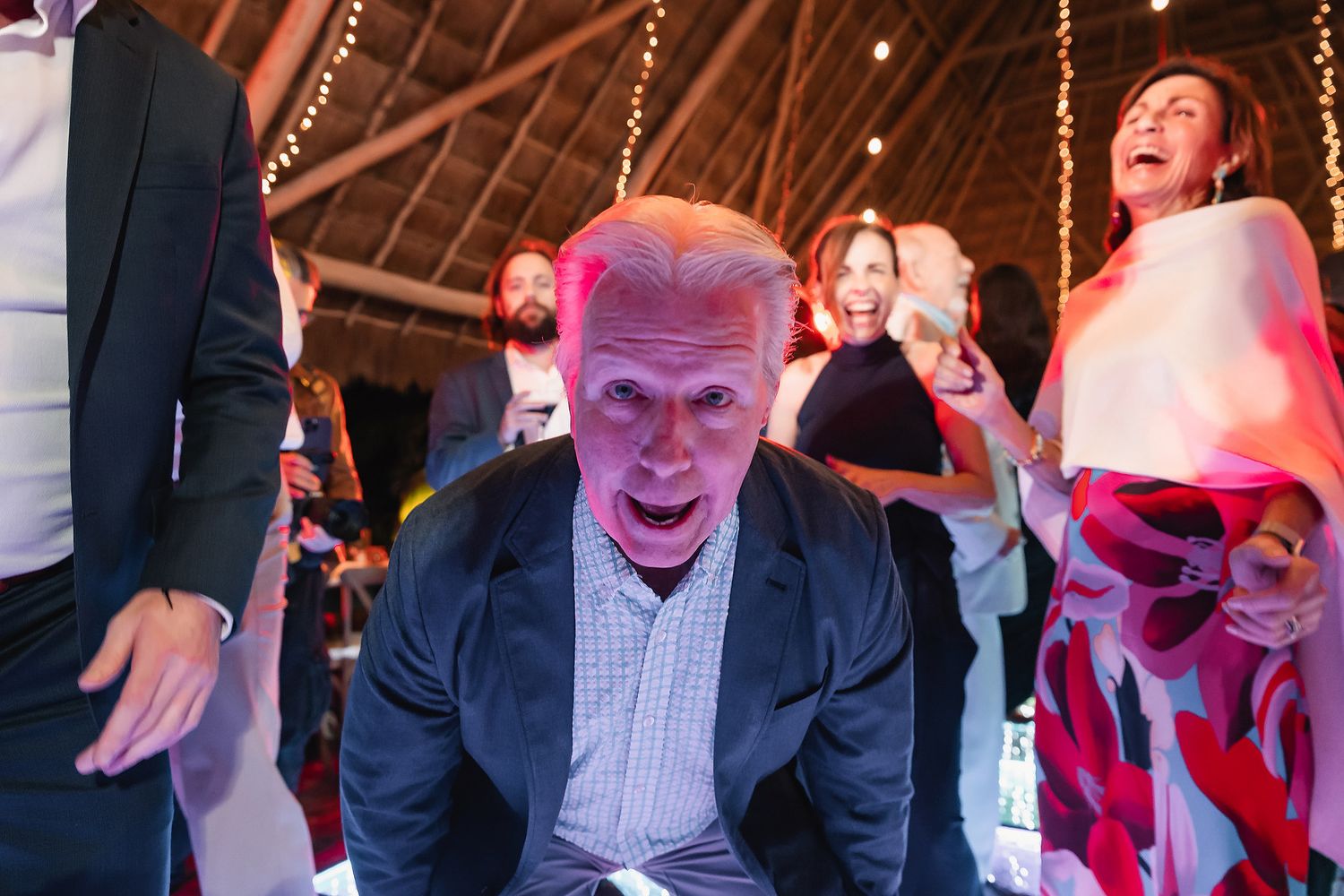 Excited man dancing at a festive indoor party with guests celebrating in the background.