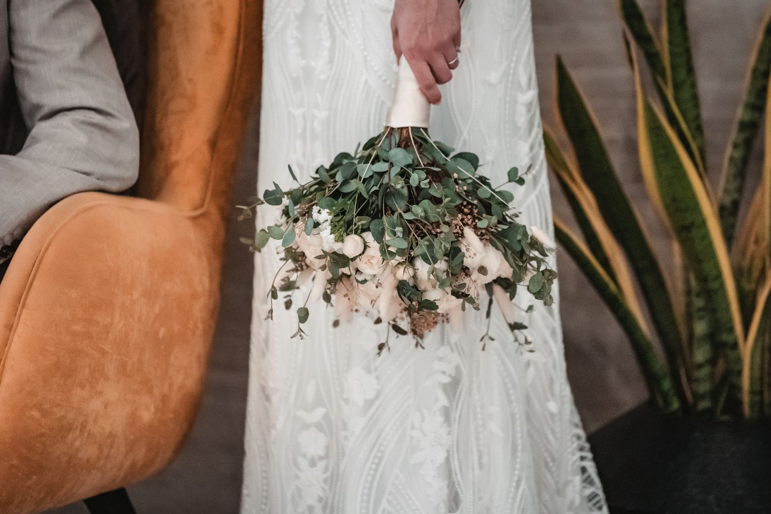 Bride in white lace gown holding cascading eucalyptus and blush floral bouquet at elegant wedding ceremony.