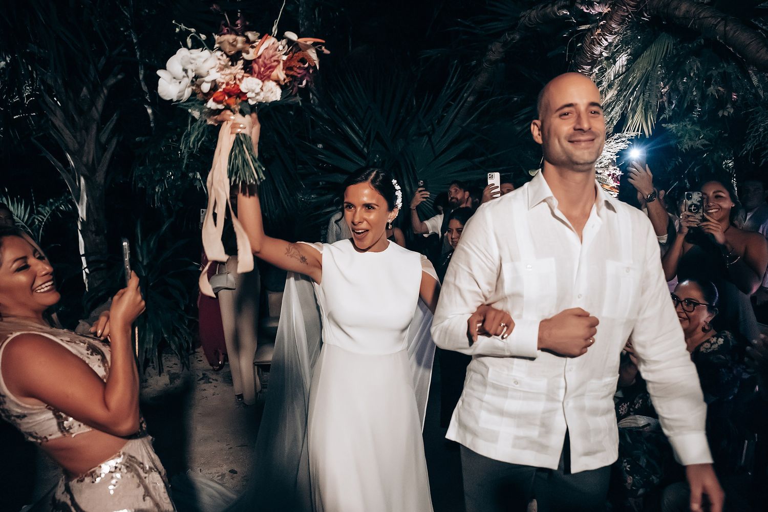 Wedding celebration with guests dancing and enjoying festivities in white attire.