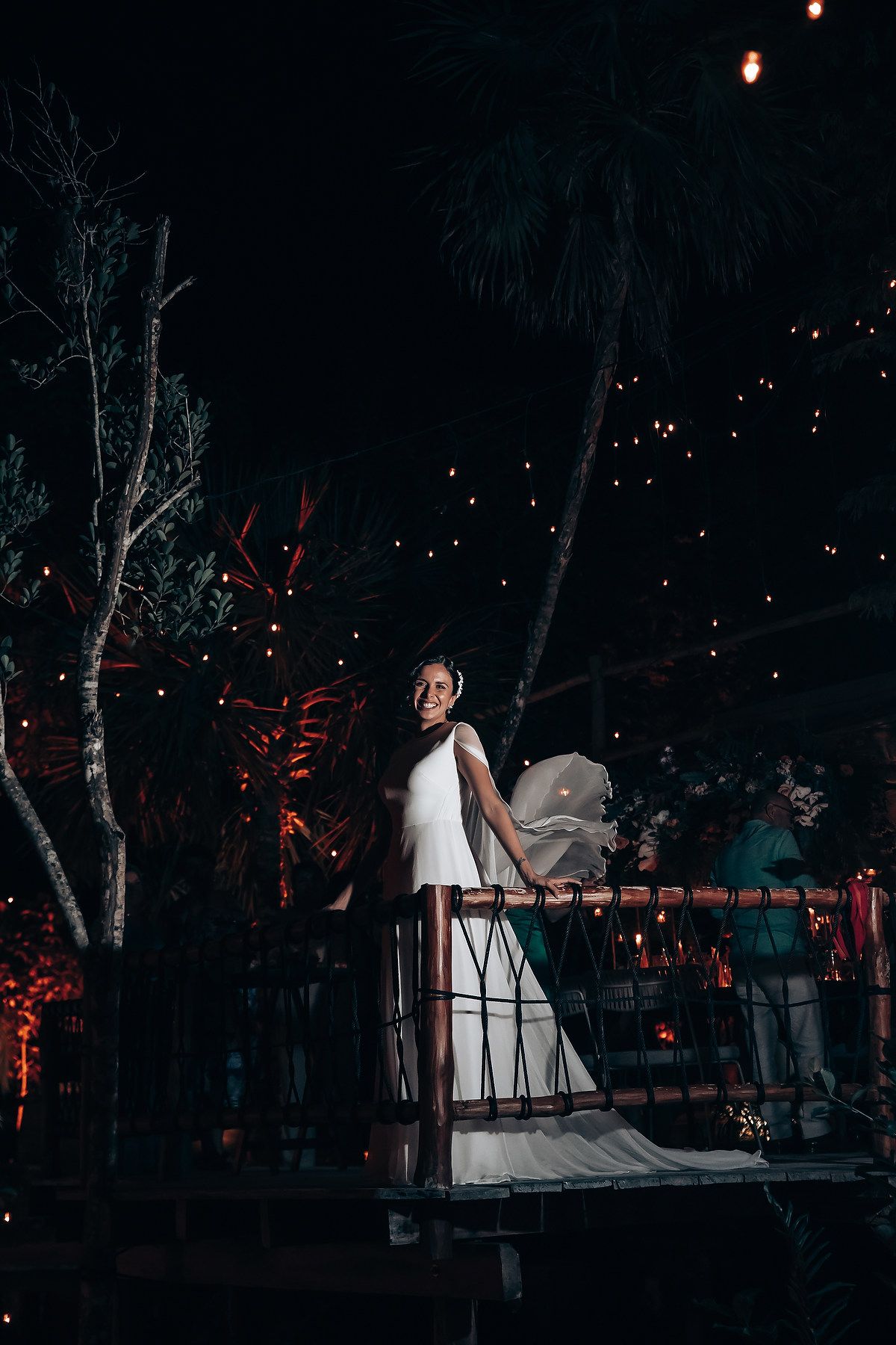 Couple shares intimate moment on outdoor deck with twinkling lights in background.