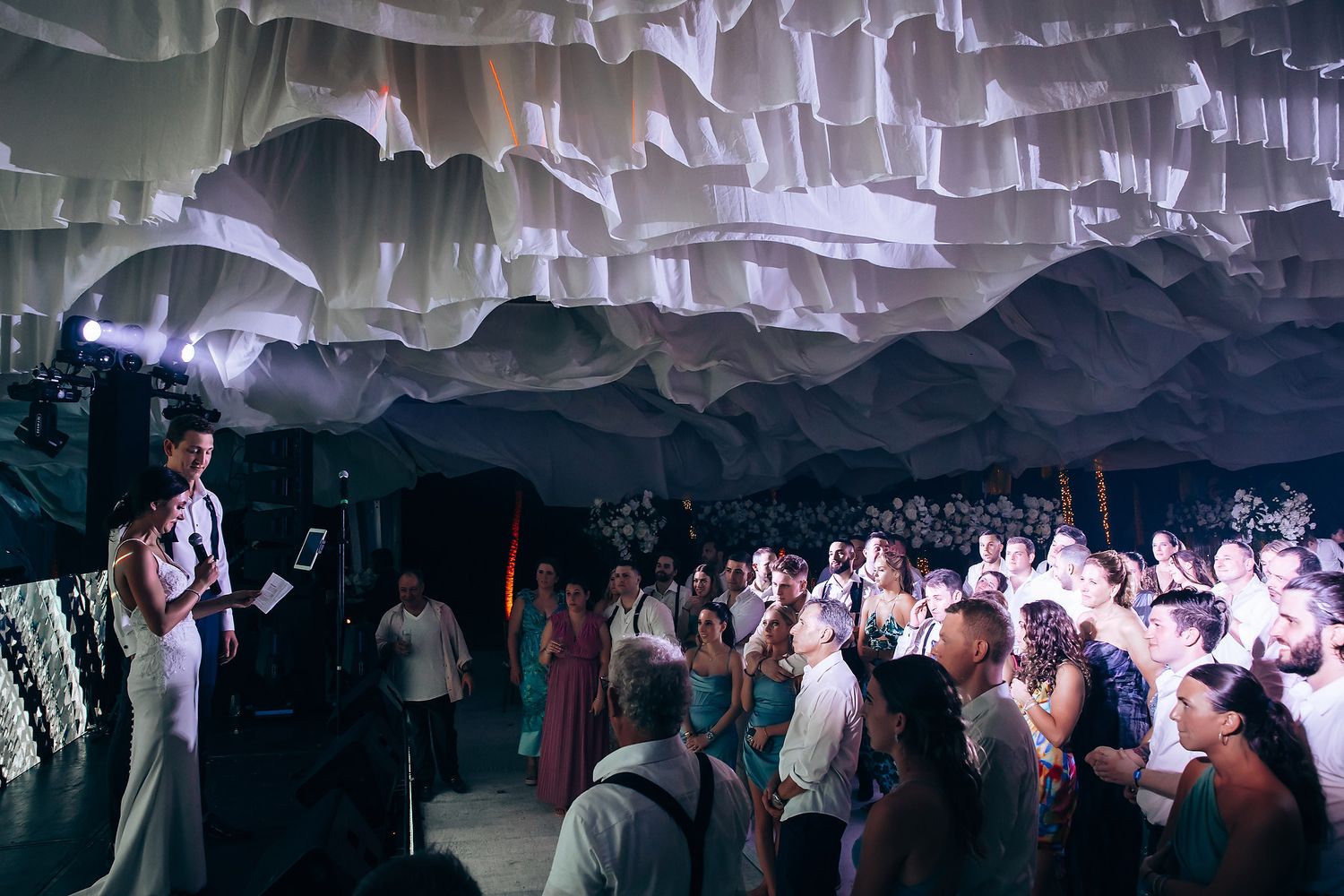 Wedding reception venue with dramatic white fabric ceiling draping and ambient lighting.