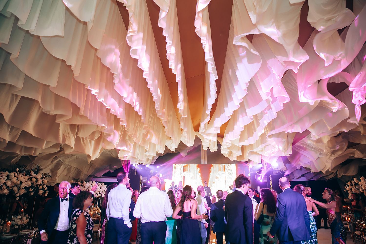 Wedding reception dance floor with dramatic draped fabric ceiling and colorful lighting.