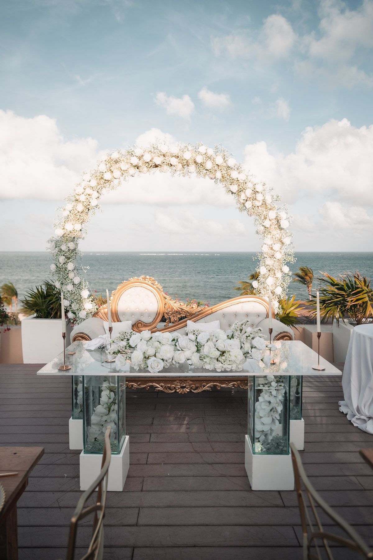 Elegant circular white floral arch frames a mirrored altar table overlooking the ocean.