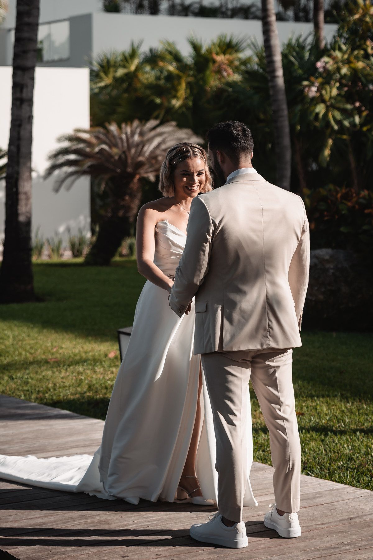 Bride and groom holding hands outdoors at tropical wedding venue surrounded by palm trees.