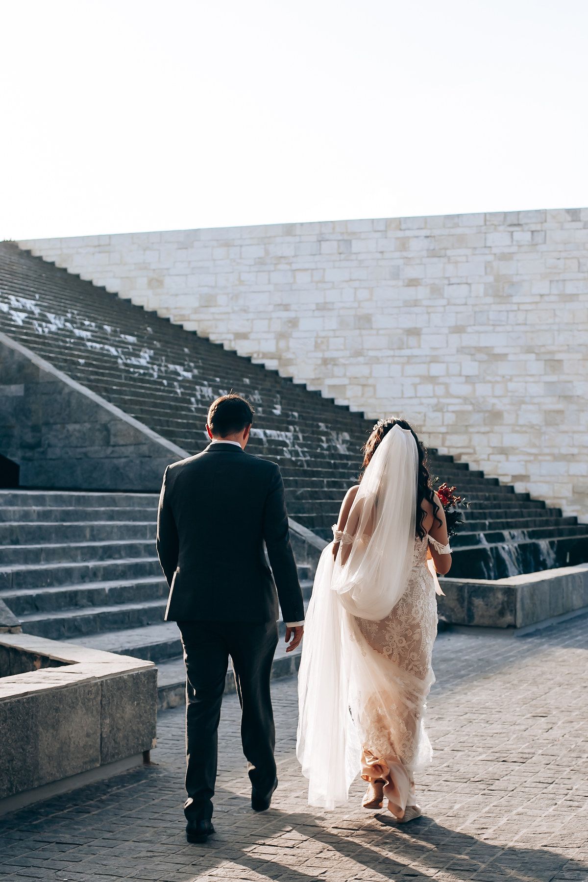 Couple in wedding attire walking up stone steps together on their special day.