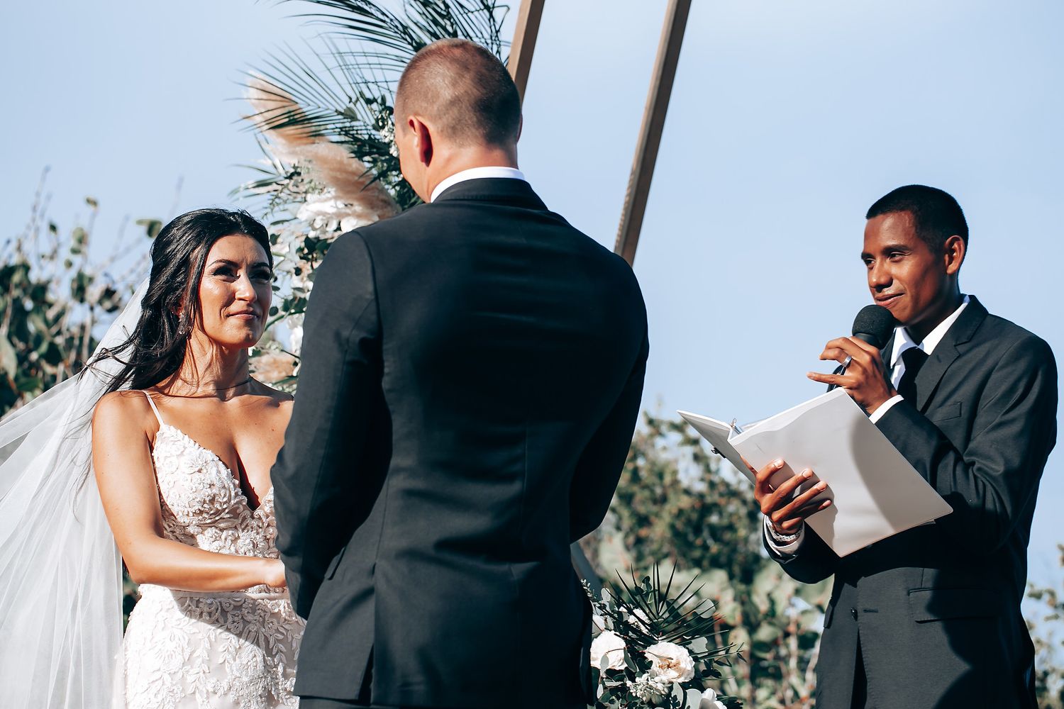 Emotional wedding ceremony moment captured against blue sky backdrop.
