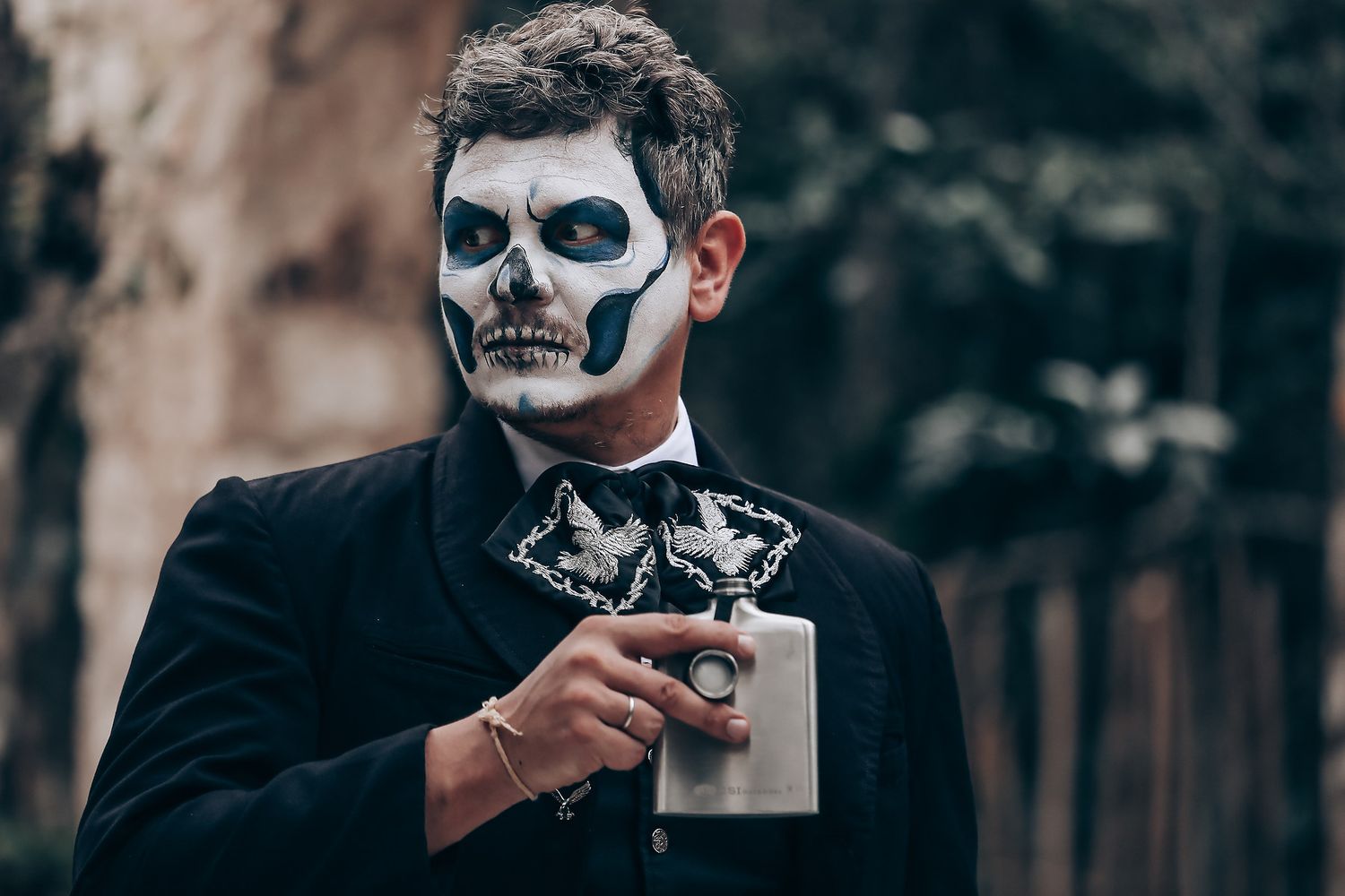 Side profile portrait showing detailed skull face paint and formal black attire.
