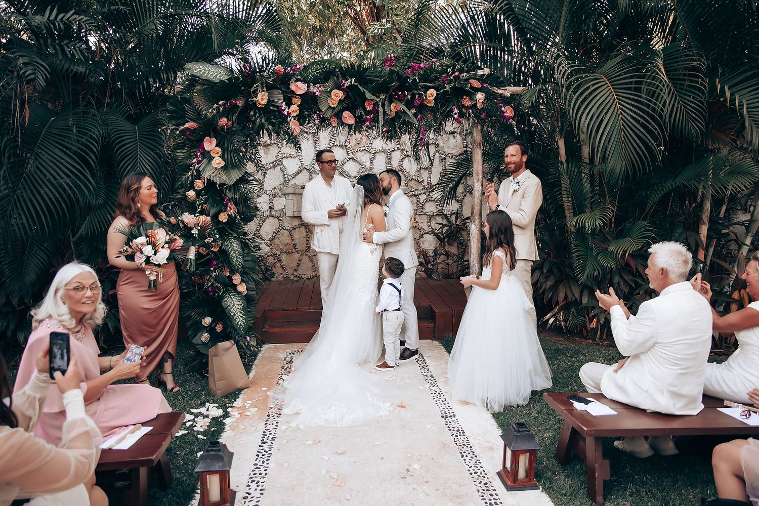 Wedding guests enjoying a reception celebration outdoors with white decor and floral arrangements.