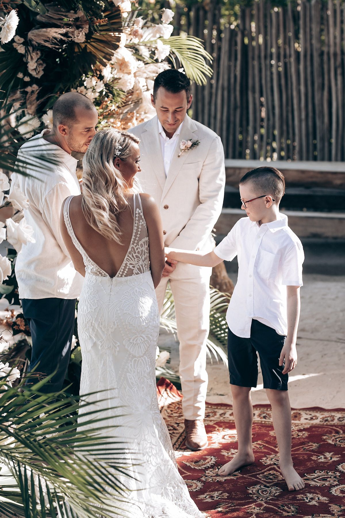 An intimate beach wedding ceremony under palm trees with tropical decor and a floral arch.