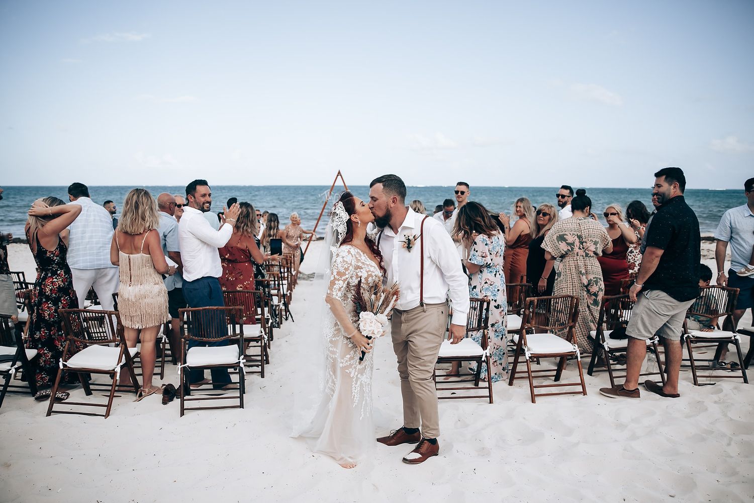 Beach wedding ceremony setup with wooden chairs facing the ocean under blue skies.