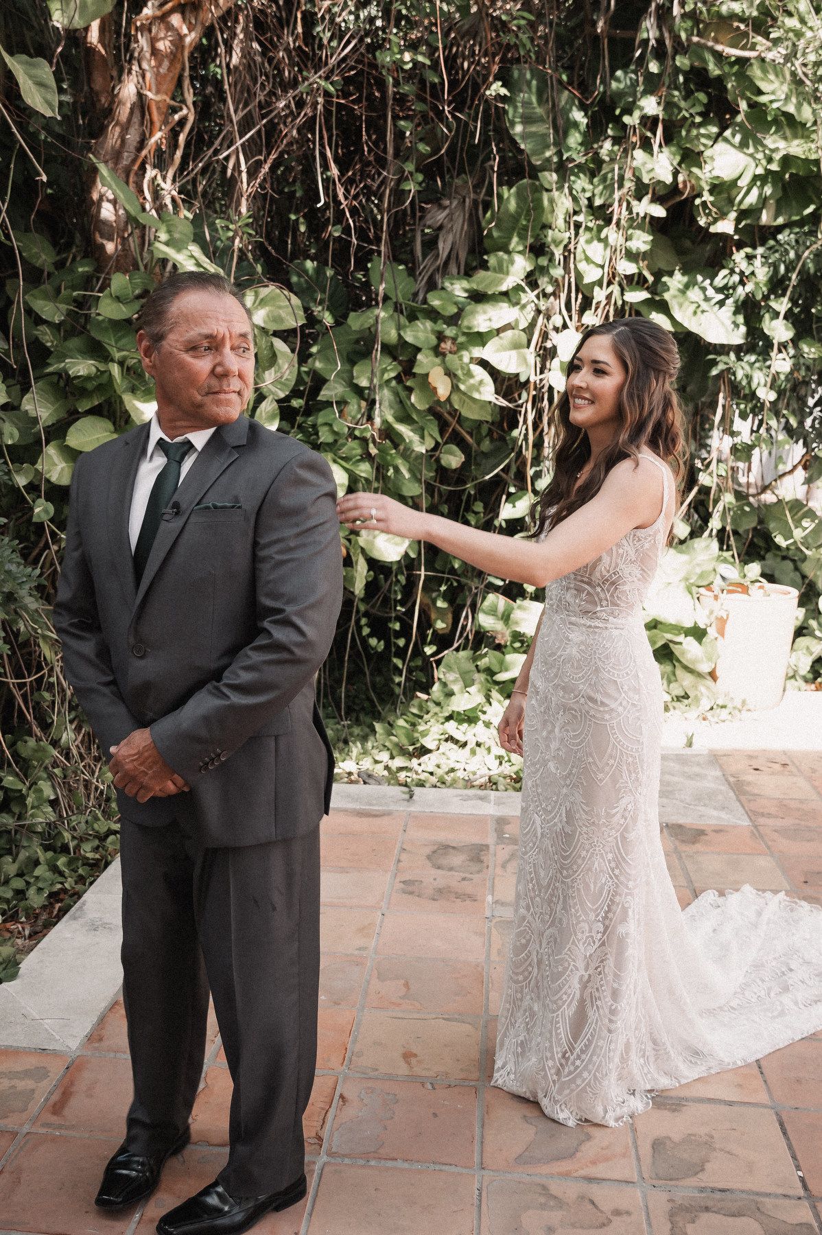 Bride in lace gown touches groom's shoulder during emotional first look at tropical garden wedding.