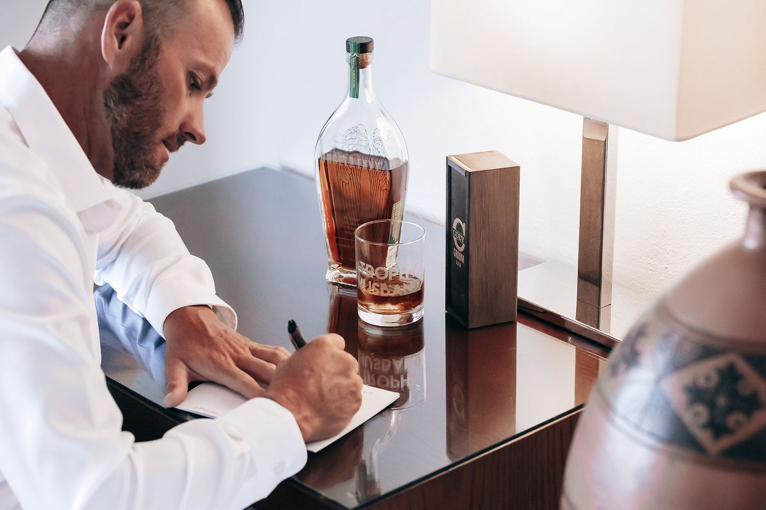 A person in a white shirt pours a glass of liquor from a bottle on a table.