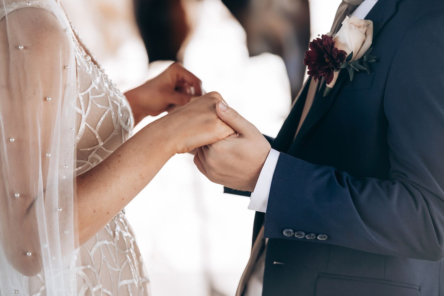 A close-up view of a bride and groom holding hands during their wedding ceremony.