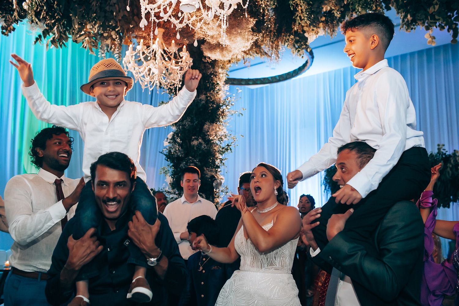Wedding celebration dance floor with guests celebrating under decorative lighting.