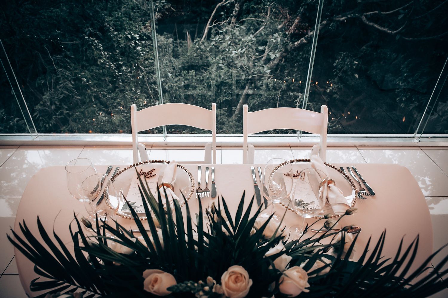 Long banquet table setup outdoors with white tablecloths and chairs for a wedding reception.