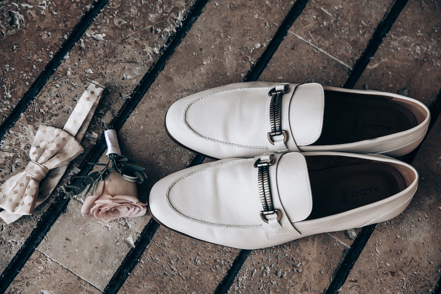White leather dress shoes placed on a textured stone surface.