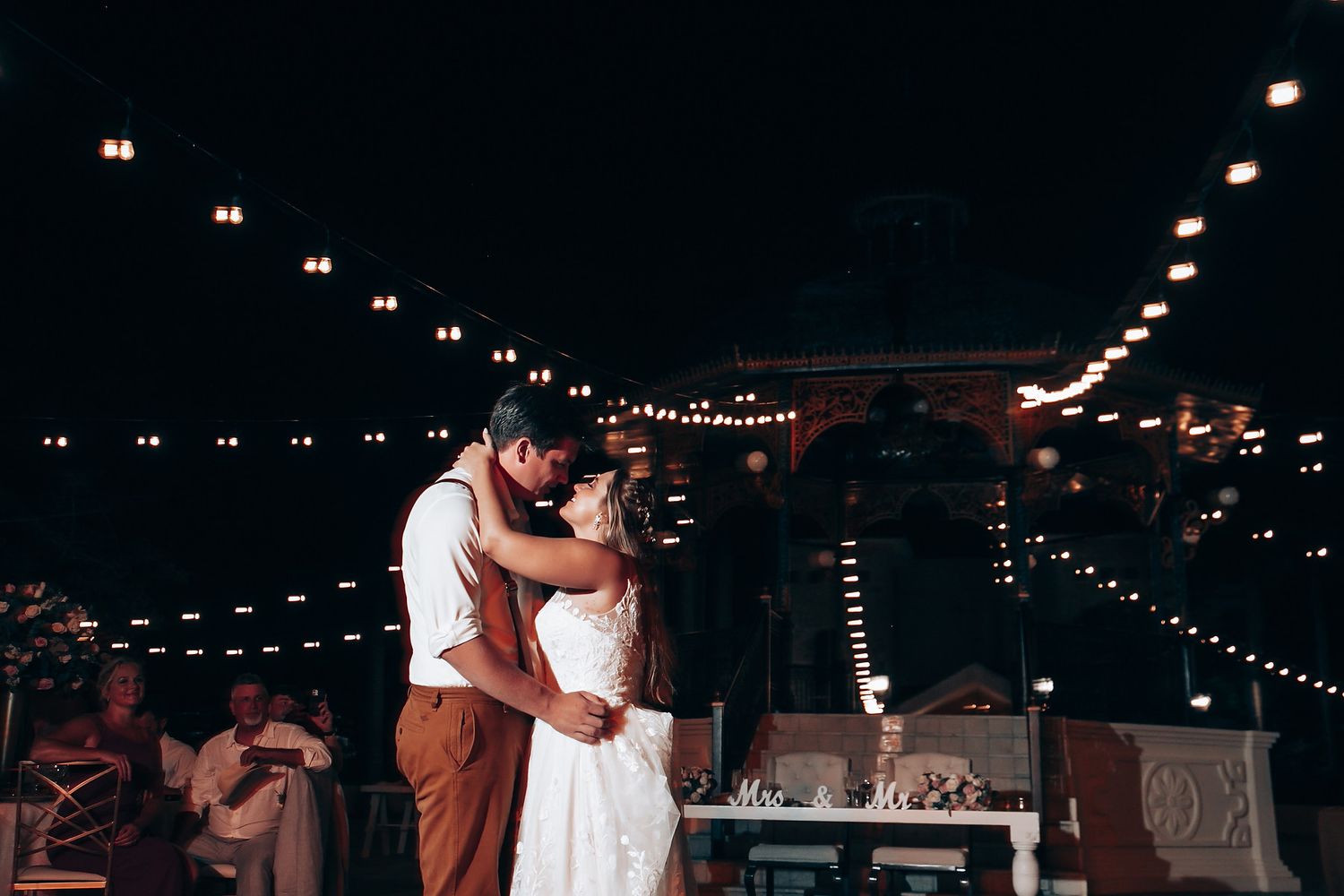 A romantic dance under twinkling string lights at an evening wedding reception.