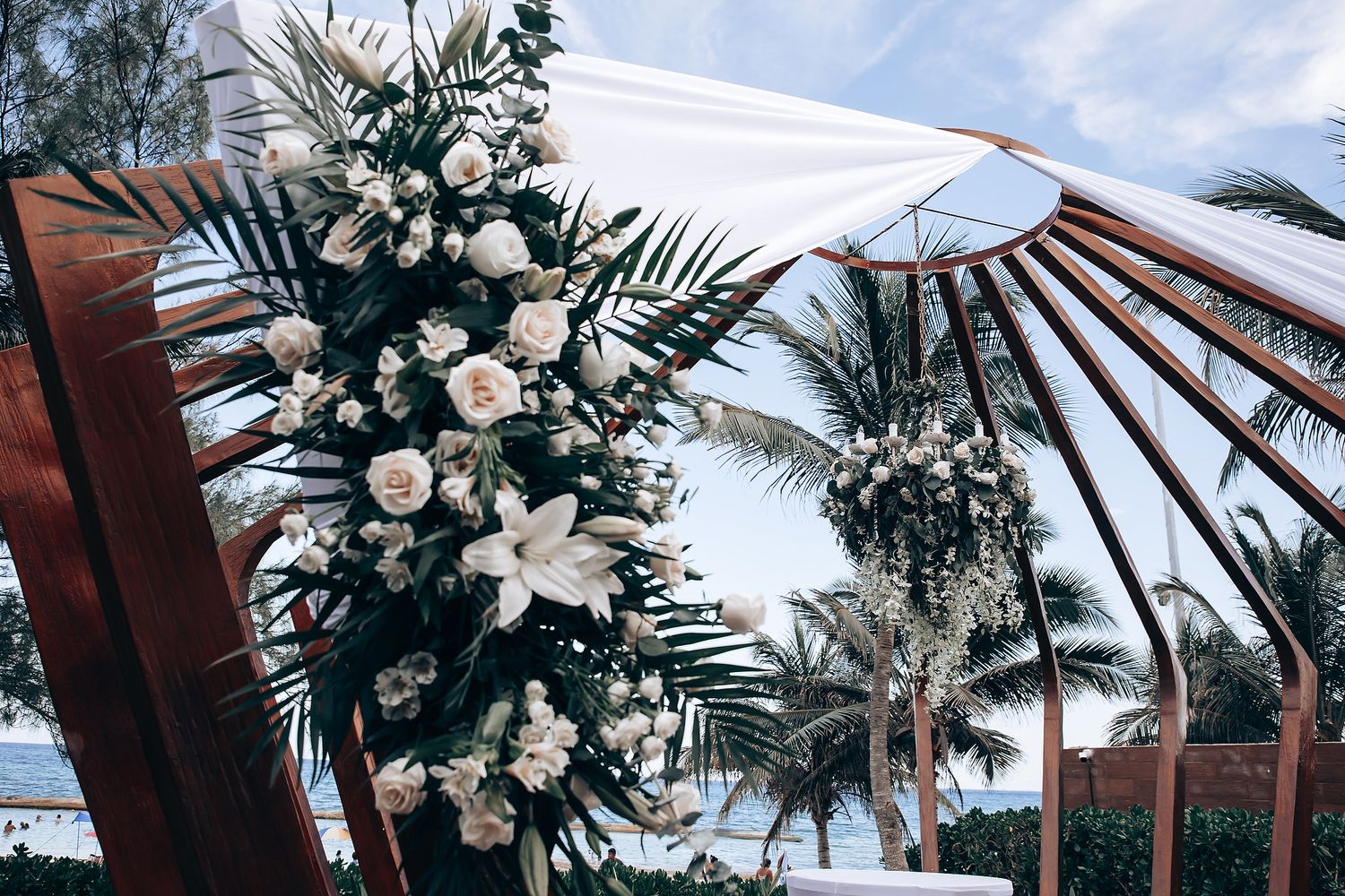 Tropical wedding ceremony setup with white floral arrangements and palm trees.