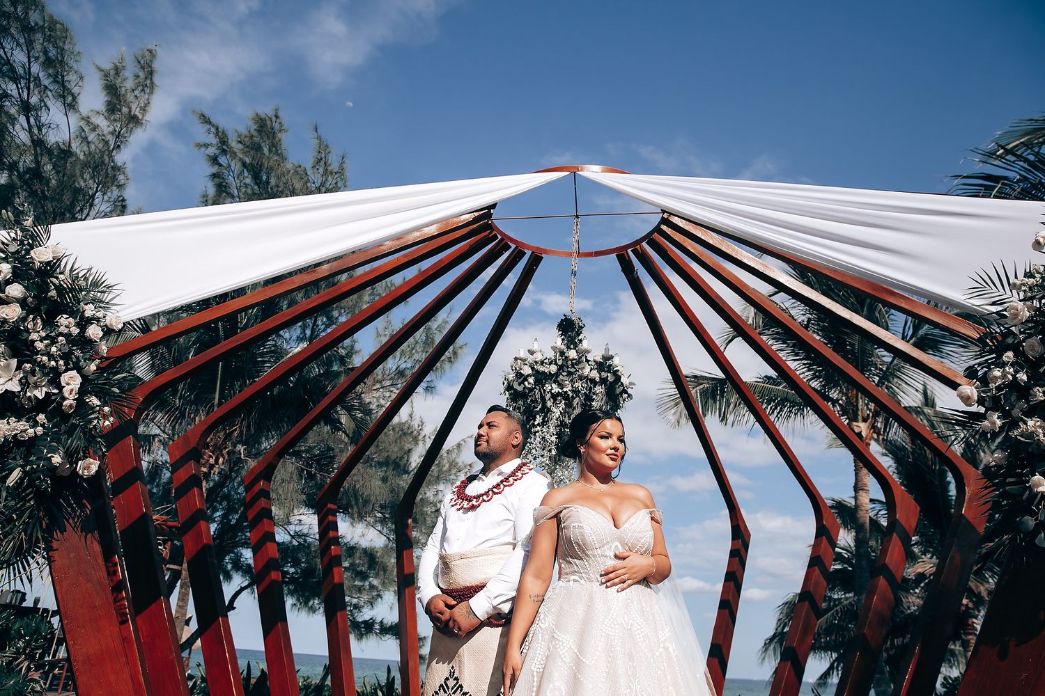 Red and white decorative umbrellas arranged in an arch against blue sky at outdoor wedding.