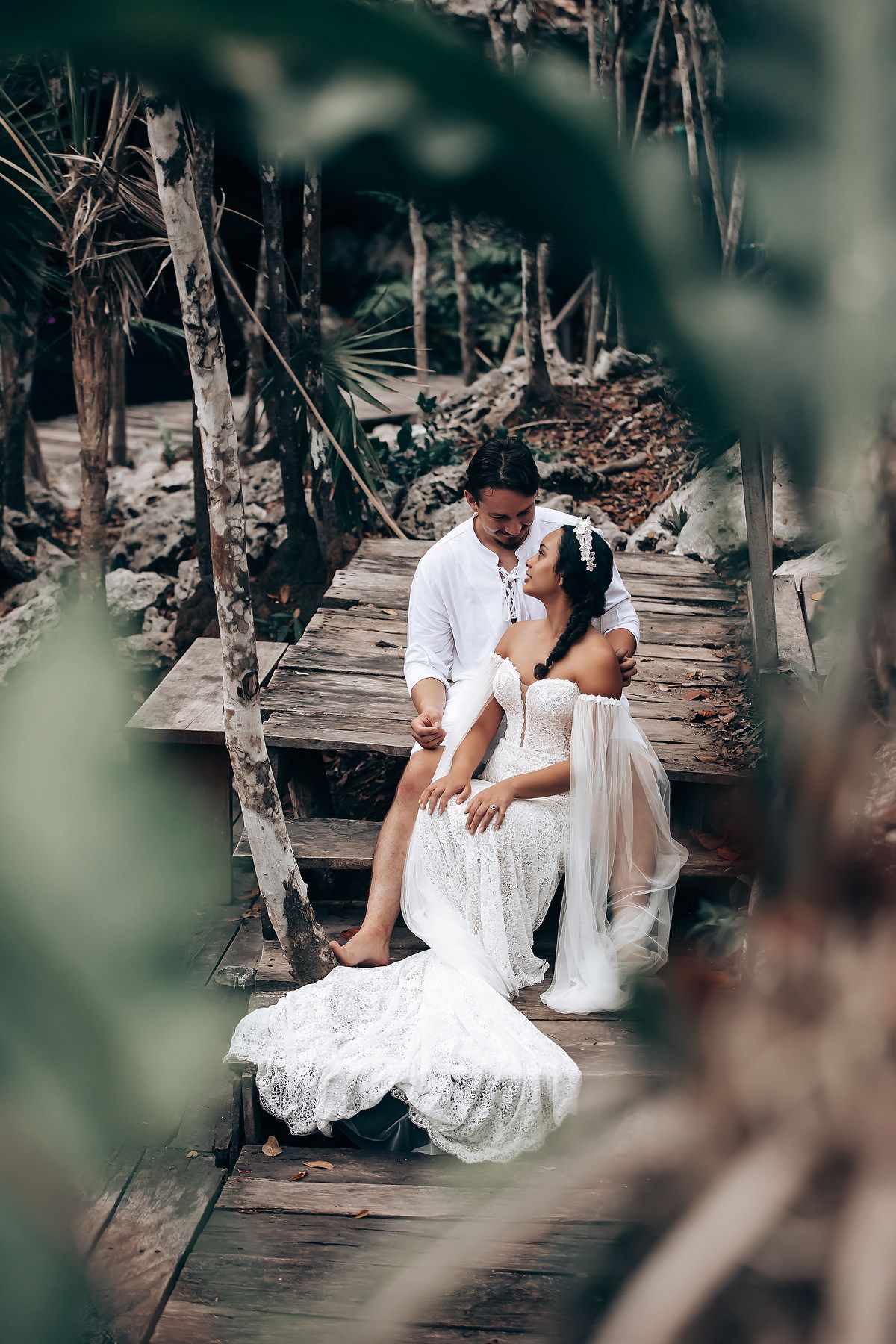 A romantic couple in white outfits shares intimate moments on a rustic wooden deck surrounded by nature.