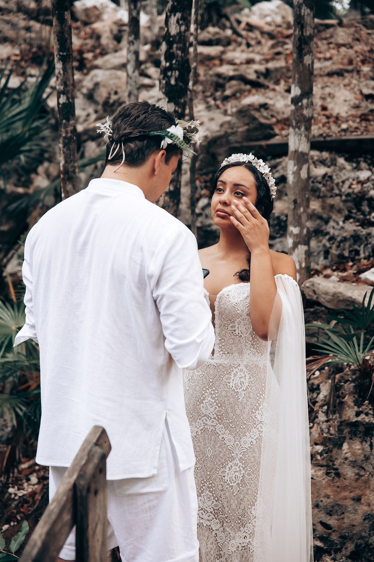 A couple shares an intimate moment during their wedding ceremony in a rustic outdoor setting with stone walls.