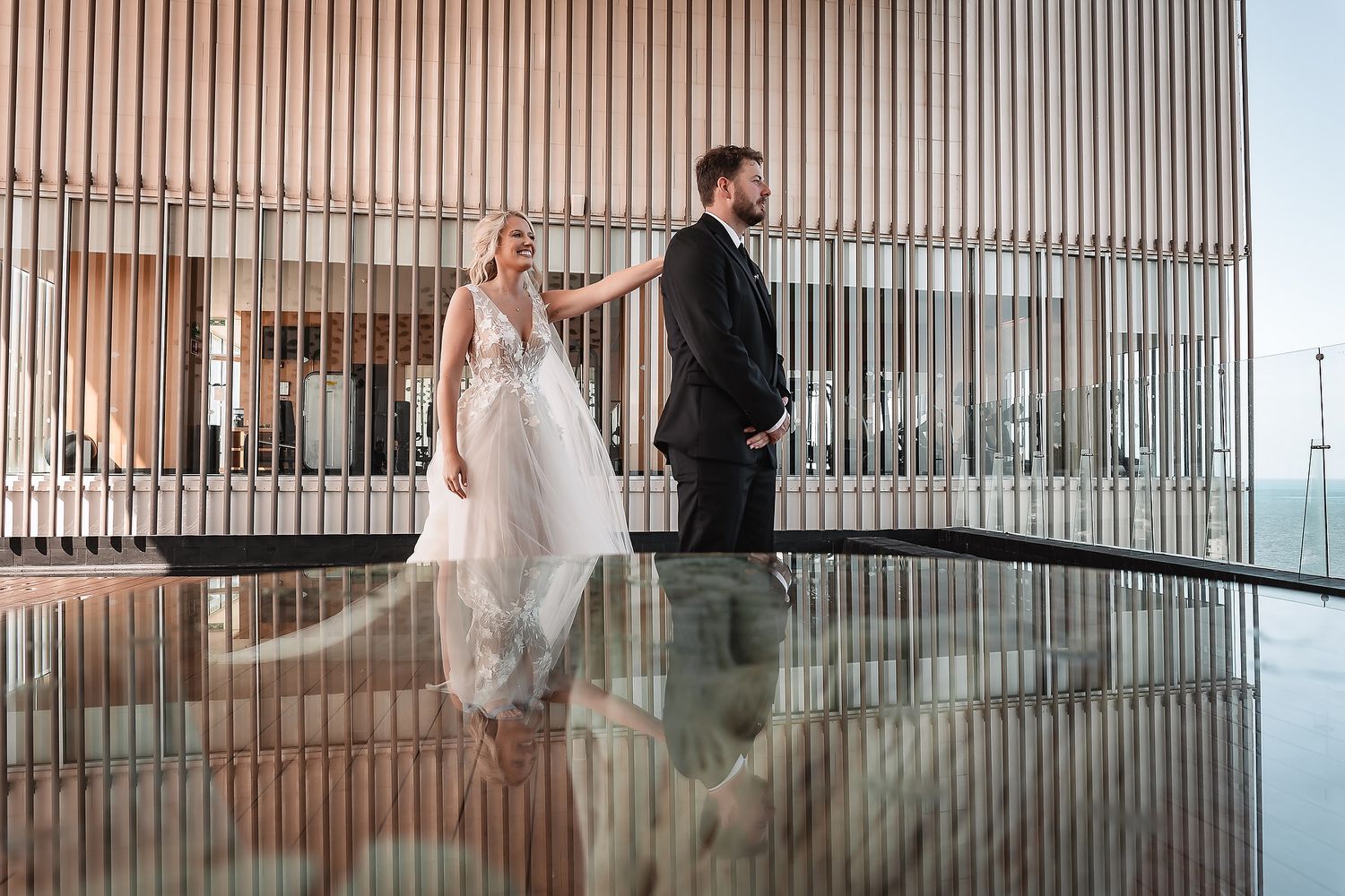 Elegant wedding couple poses on a modern balcony with glass railings and wooden details.