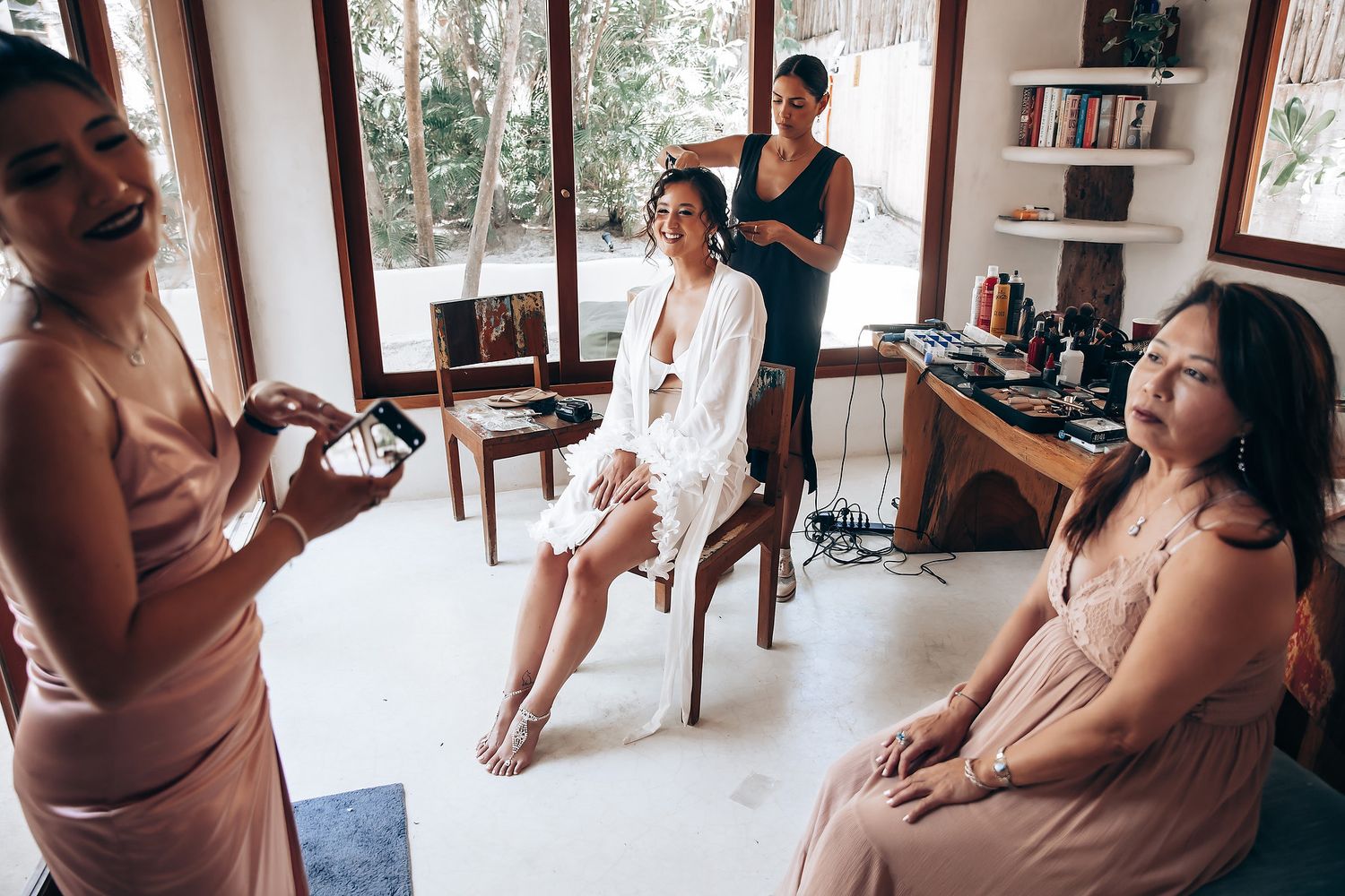 Bridesmaids in dusty rose dresses prepare for a wedding in an elegant indoor setting.