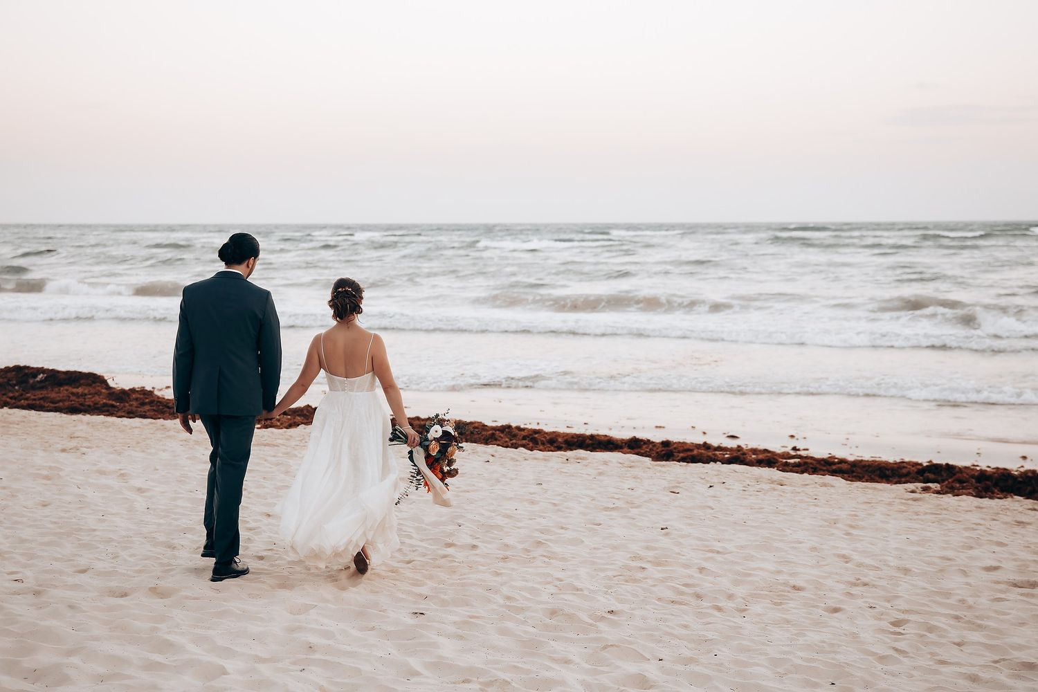 Couple walking along beach shoreline during sunset.
