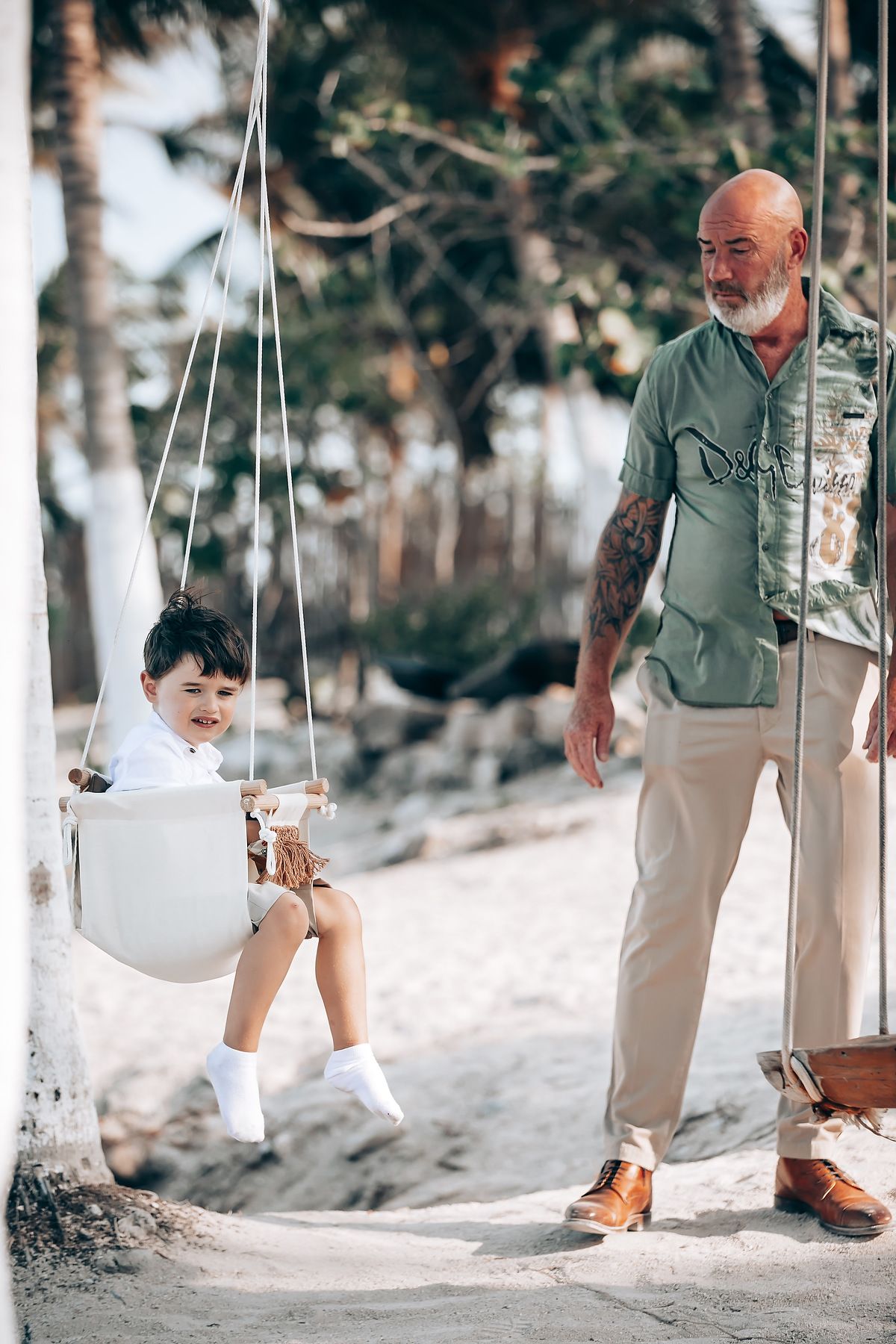 A person pushes a child on a white swing set in a snowy winter forest setting.