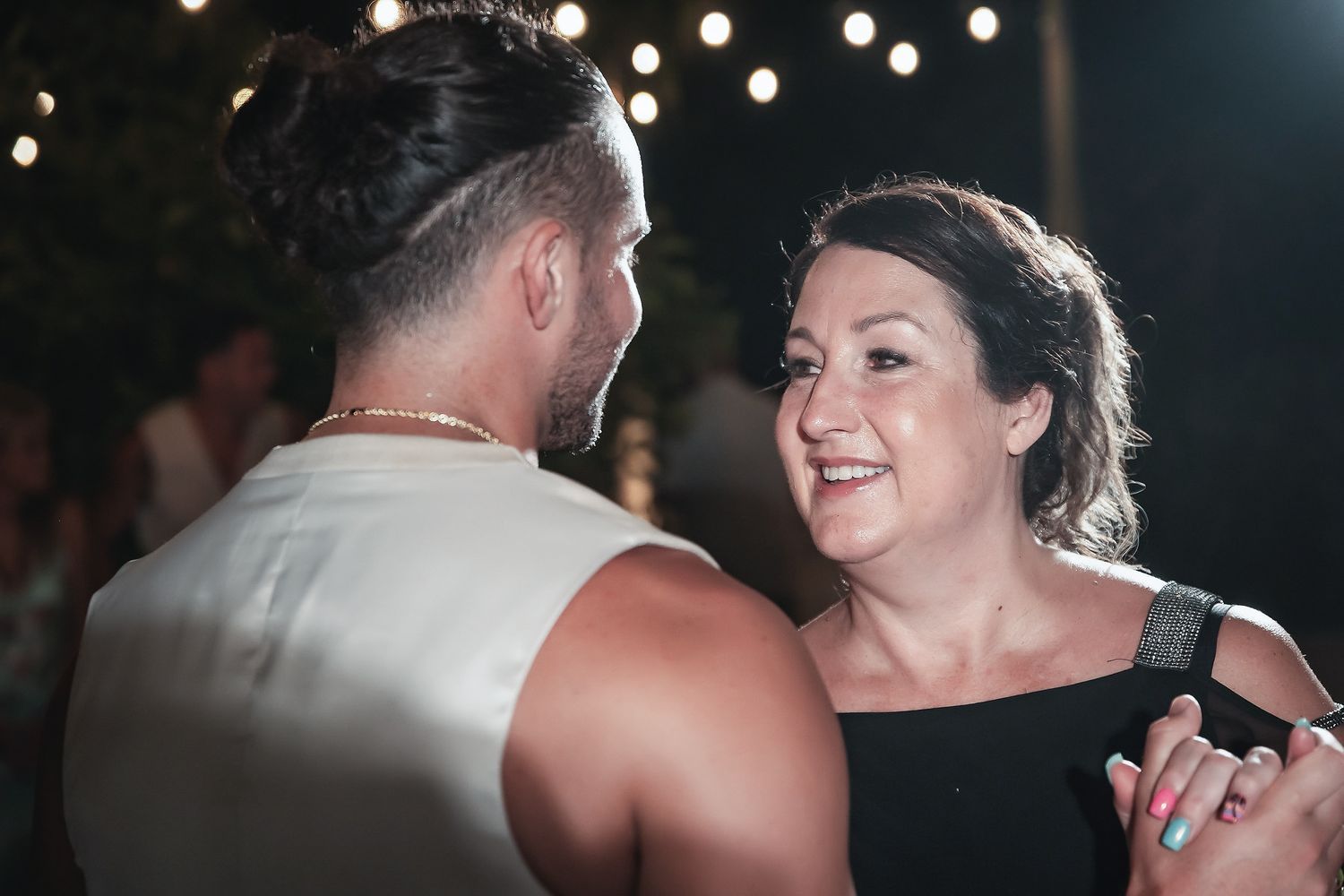 Couple sharing a romantic dance at an outdoor evening event with string lights glowing in the background.