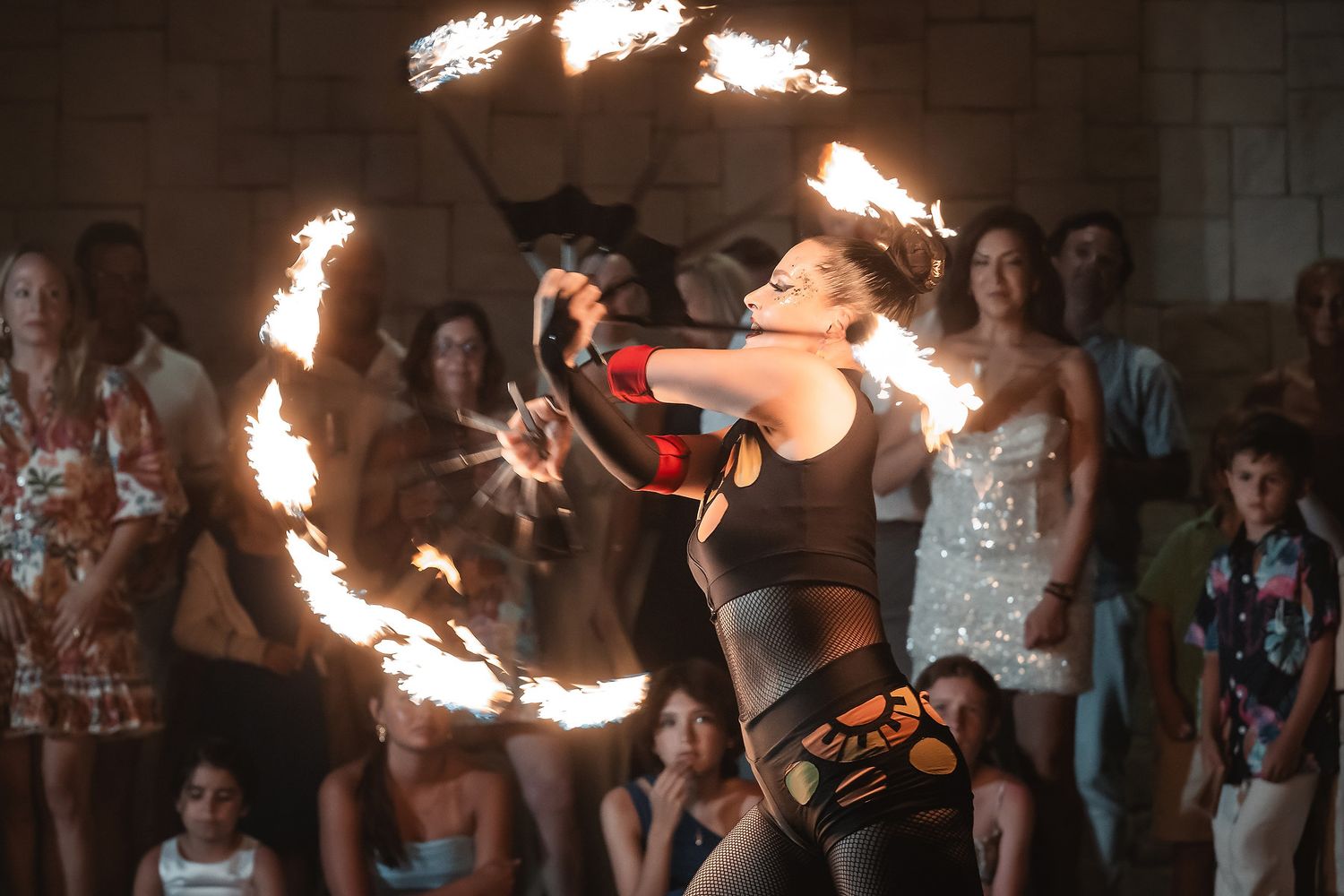 Fire dancer performing with spinning flames for a crowd at an outdoor evening event.